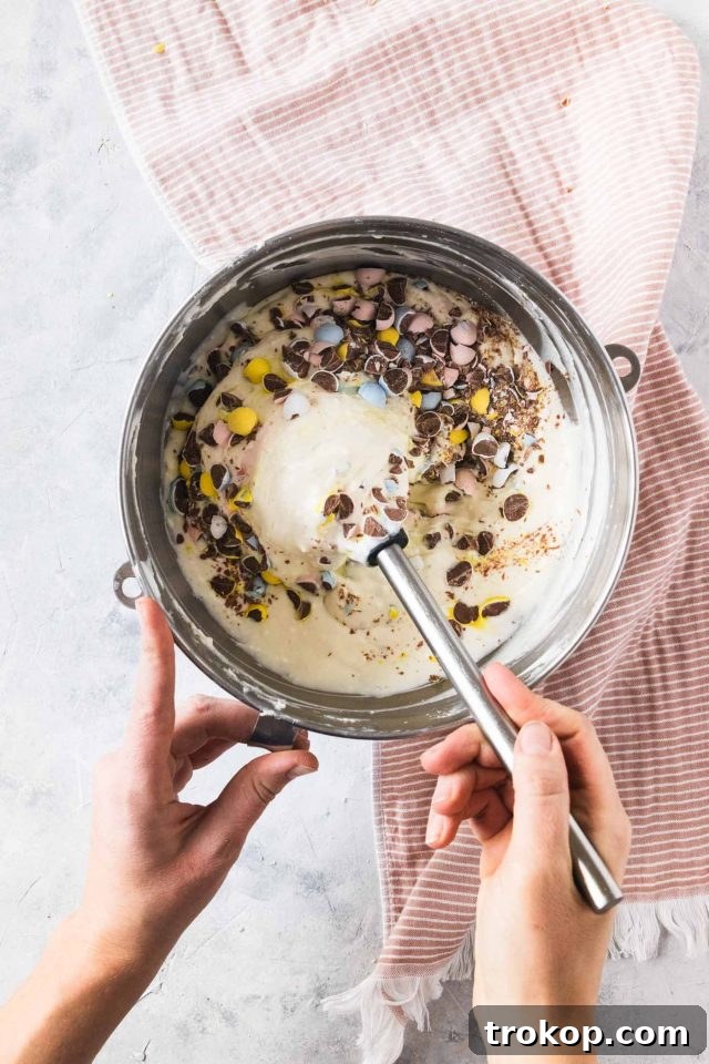 A close-up of mini Cadbury eggs being chopped into the creamy cheesecake filling mixture in a large bowl