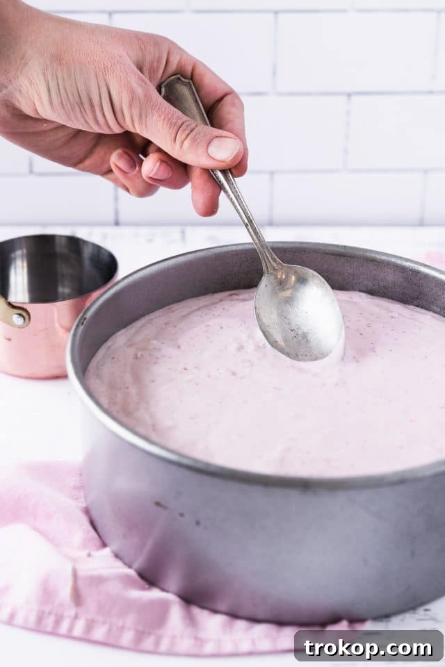 A photo demonstrating the correct way to place a low-carb strawberry cheesecake into a water bath for even baking, showing the foil-wrapped pan in a larger dish.