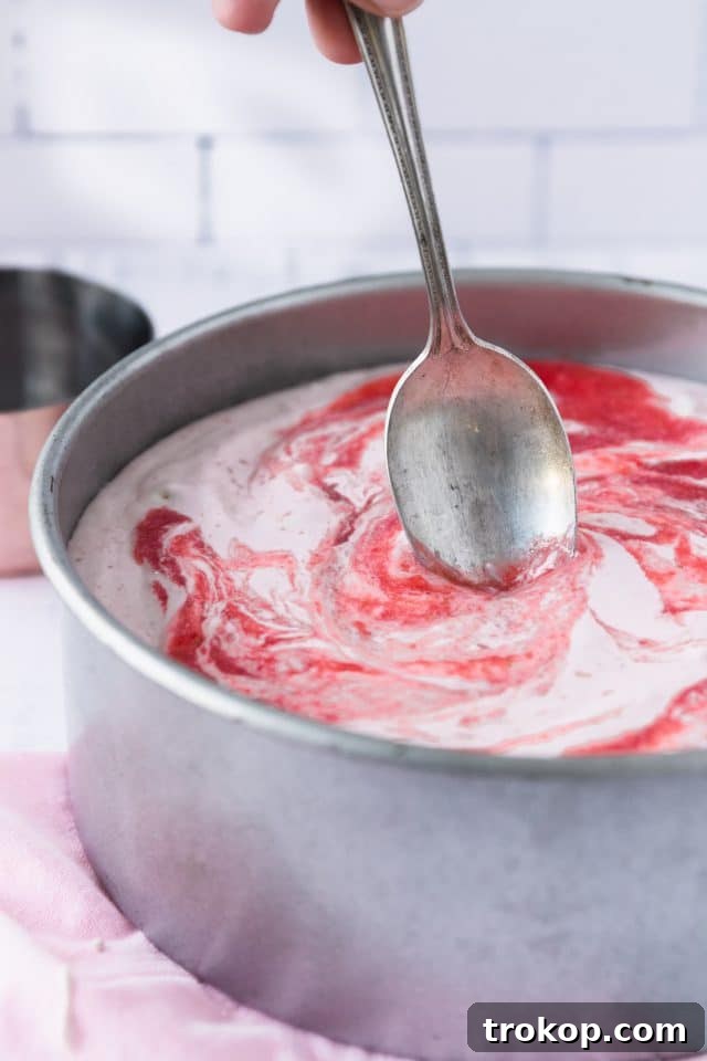 A close-up shot of the vibrant strawberry puree being poured into the low-carb cheesecake batter, showing the colorful addition.