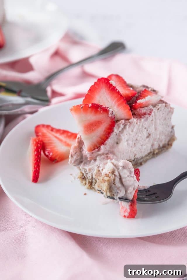 A close-up photograph of a single slice of keto strawberry cheesecake, showing its perfectly set texture, distinct layers, and fresh strawberry garnish.