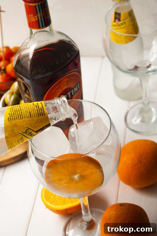 The Ultimate Martini Fiero Recipe 6 Tonic water being poured into a glass with ice and an orange slice, ready for Martini Fiero.
