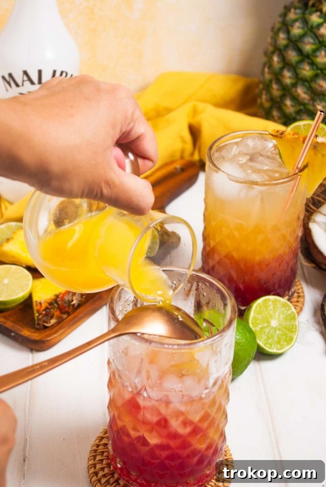 Perfect Tropical Malibu Bay Breeze Mix 5 Ingredients and bar tools laid out on a table, including Malibu rum, pineapple juice, cranberry juice, a highball glass, and a spoon for making a Malibu Bay Breeze.