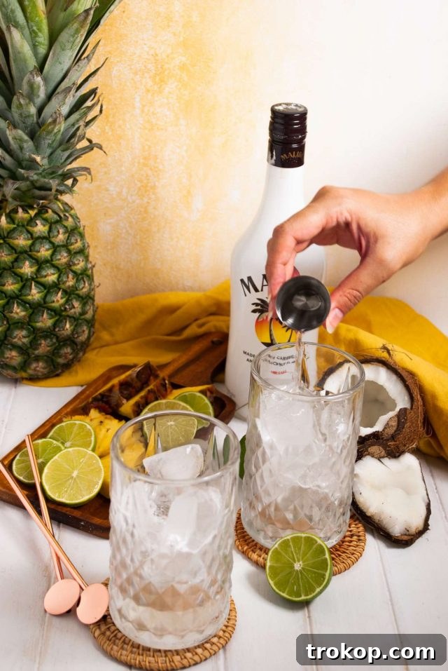 Perfect Tropical Malibu Bay Breeze Mix 6 Two hands preparing a Malibu Bay Breeze cocktail, pouring pineapple juice over a spoon to create layers, with ingredients and glassware neatly laid out on a clean surface.