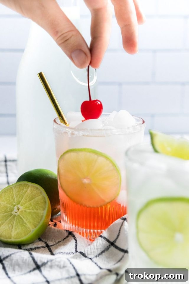 Refreshing Homemade Limeade 3 Hand placing a fresh cherry on top of a vibrant cherry limeade drink, showcasing garnishing techniques.