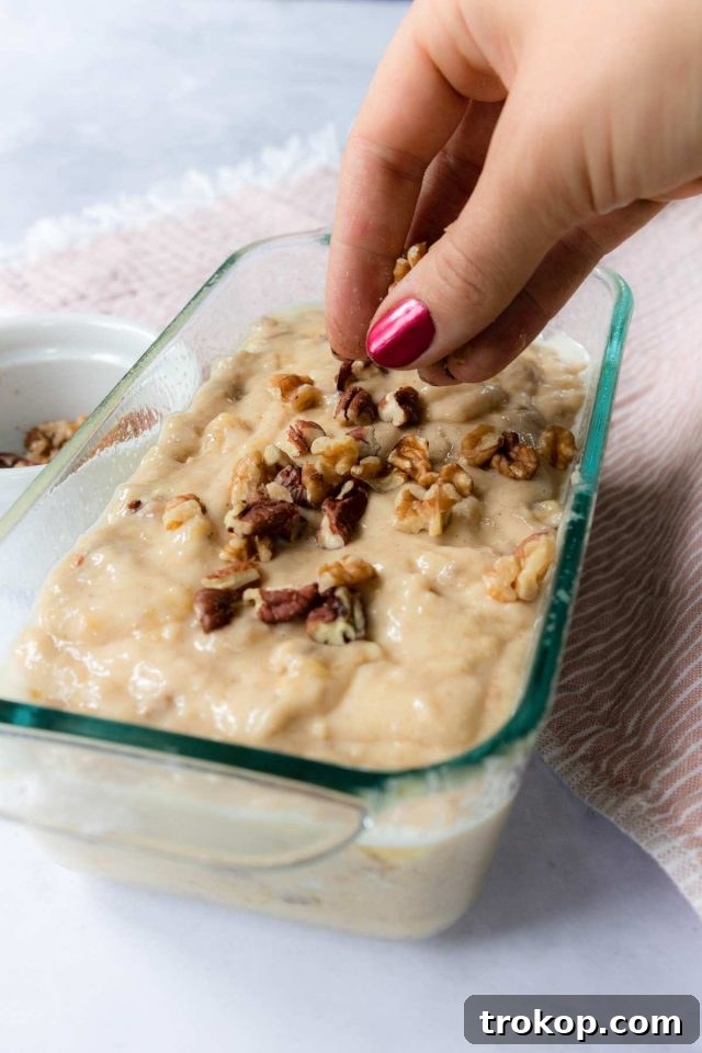 Banana bread batter poured into a greased loaf pan, with nuts sprinkled on top.