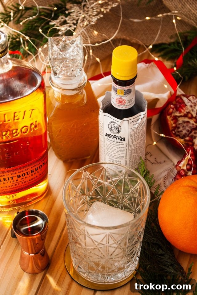 Heirloom Christmas Recipes 6 A Christmas Old Fashioned cocktail being garnished with an orange peel and pomegranate seeds.
