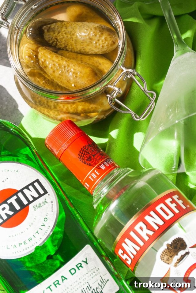 Ingredients laid out for a dill pickle martini, including vodka, vermouth, pickle juice, and fresh pickles.