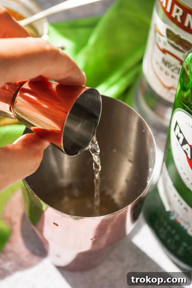 A cocktail shaker being filled with ice and liquids to make a pickle martini recipe.