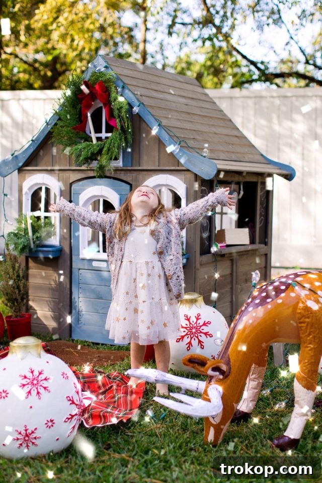 Two children playing outside a decorated playhouse, one holding a gingerbread cookie