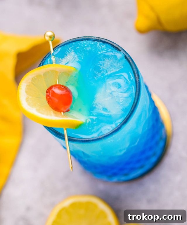 A refreshing glass of Blue Motorcycle cocktail, garnished with a lemon slice and a vibrant cherry, sitting on a wooden surface.