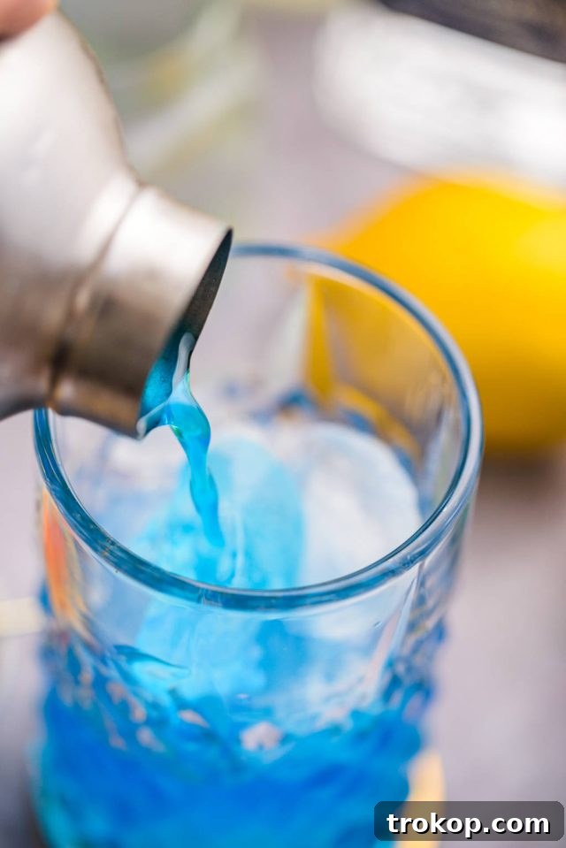 Pouring the Blue Motorcycle cocktail mixture into a tall glass filled with crushed ice