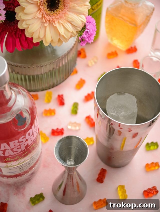 A hand preparing Gummy Bear Shots, pouring the mixture from a shaker into a glass with gummy bears