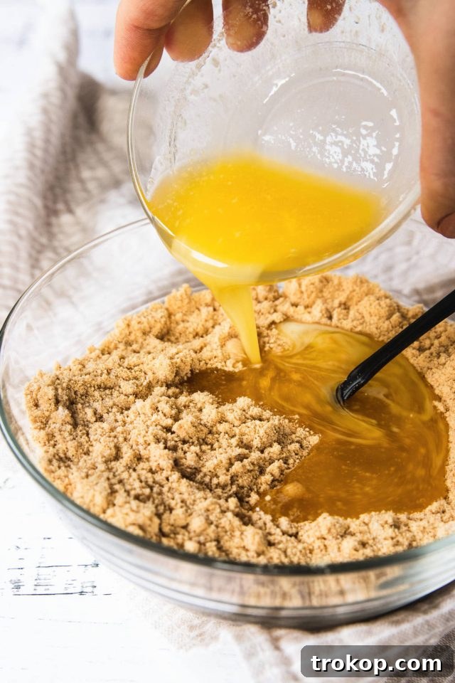 Decadent Baked Caramilk Cheesecake 4 Pouring the melted butter into the graham cracker crumbs in a mixing bowl for the Caramilk Cheesecake recipe