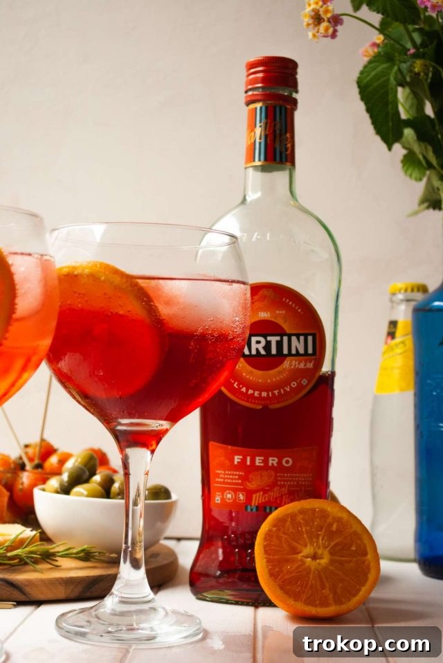 Shake It Up 11 Vodka Martini Variations 8 A vibrant Fiero Martini, garnished with a slice of orange, served over ice in a tall glass.