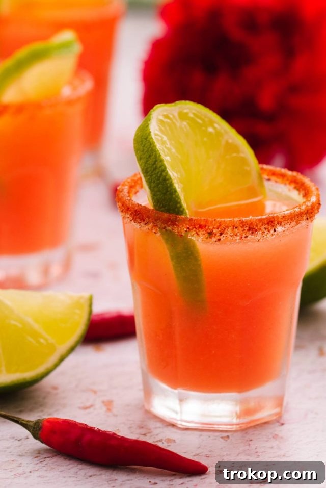 A vibrant Mexican Candy Shot garnished with a lime wedge and chili powder rim.
