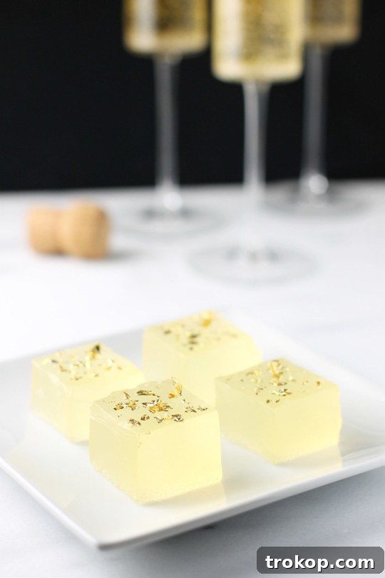A plate of sparkling champagne jello shots adorned with edible gold, with champagne coupes in the background.