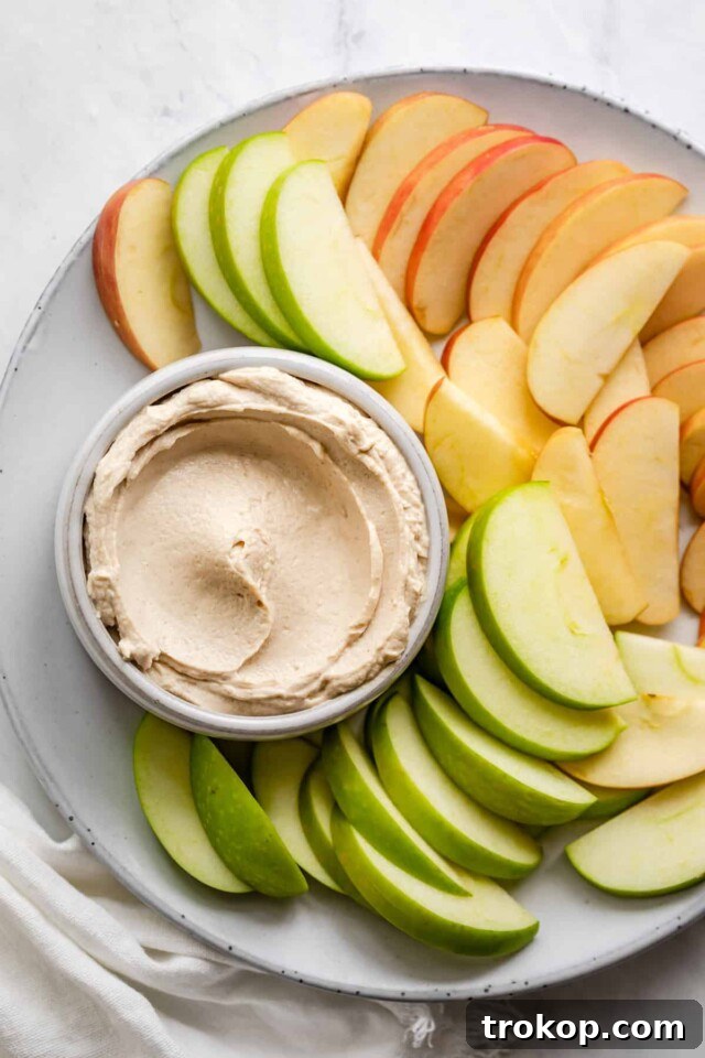 Crave-Worthy Peanut Butter Desserts You Need to Bake 6 A bowl of creamy peanut butter dip, garnished with nuts and surrounded by fruit slices and pretzels.