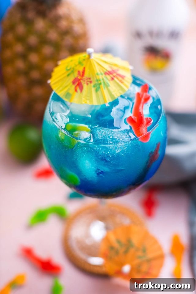 A vibrant blue Fish Bowl Drink, garnished with colorful Swedish Fish candies and a cocktail umbrella, ready to be served at a party.