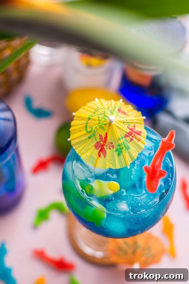 A top-down view of a Fish Bowl Drink cocktail in a large glass, garnished with an umbrella and Swedish Fish, highlighting its appealing presentation.