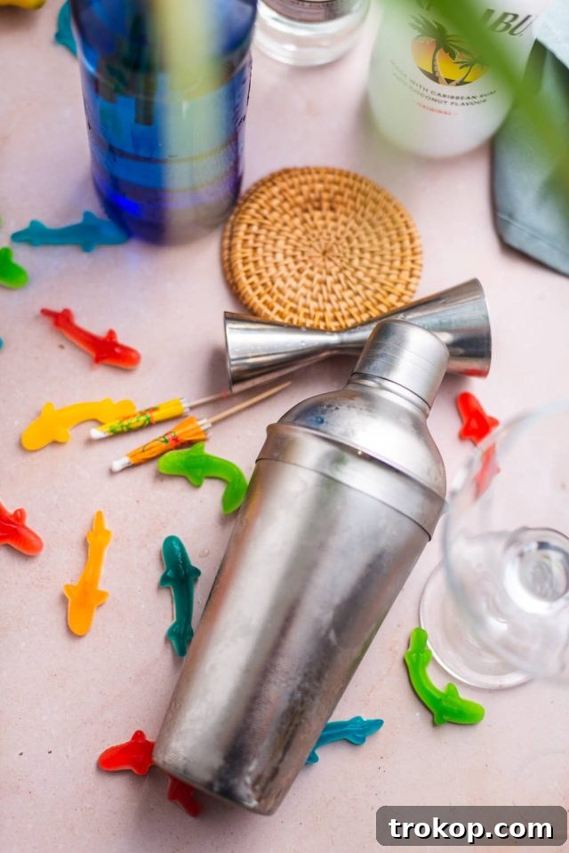 A collection of essential bar equipment for making cocktails, including a balloon glass, cocktail shaker, jigger, and cocktail umbrella picks.