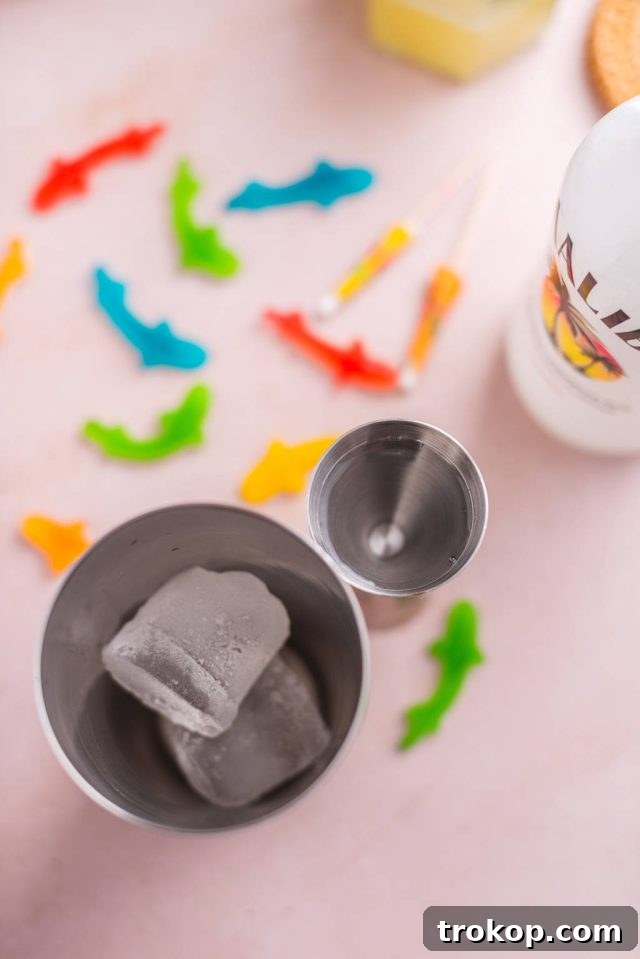 A cocktail shaker being filled with ice cubes, ready for mixing the Fish Bowl Drink ingredients.