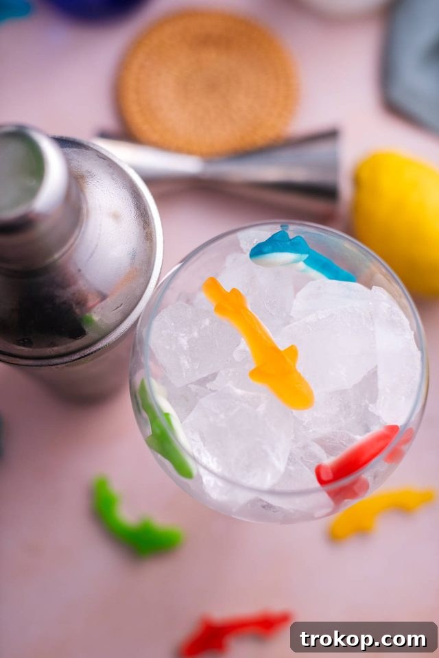 Placing colorful Swedish Fish candies into a balloon glass filled with crushed ice, illustrating the preparation step for the Fish Bowl Drink.