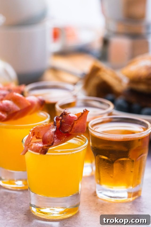 Glasses of the Breakfast Shots lined up, each topped with a perfectly cooked strip of bacon.