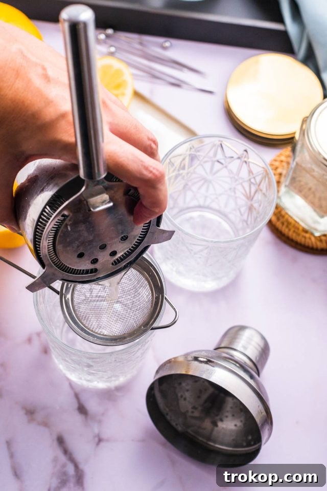 Straining the Vodka Sour cocktail into a glass through a fine mesh strainer