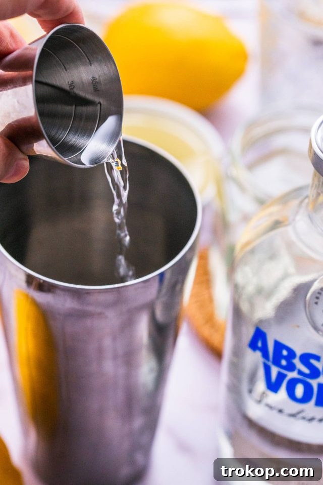 Pouring vodka into a cocktail shaker with other ingredients for a Vodka Sour