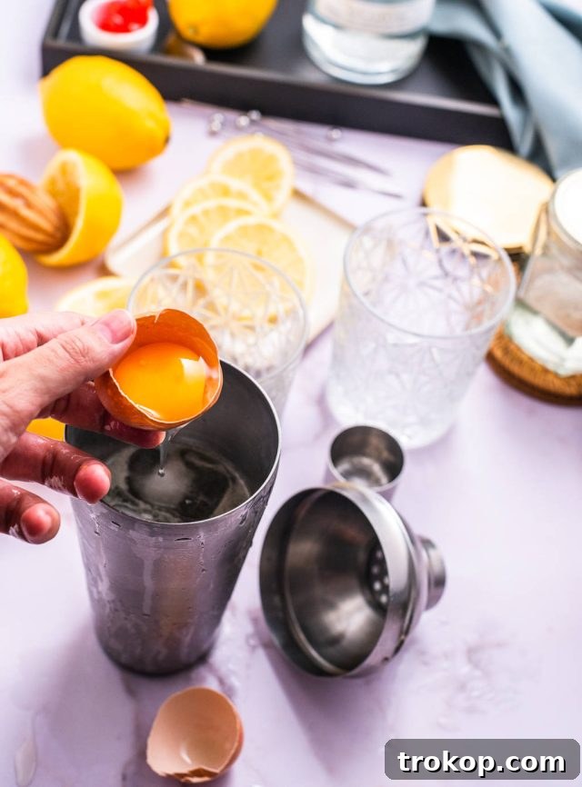 Carefully adding an egg white into a cocktail shaker for a frothy Vodka Sour