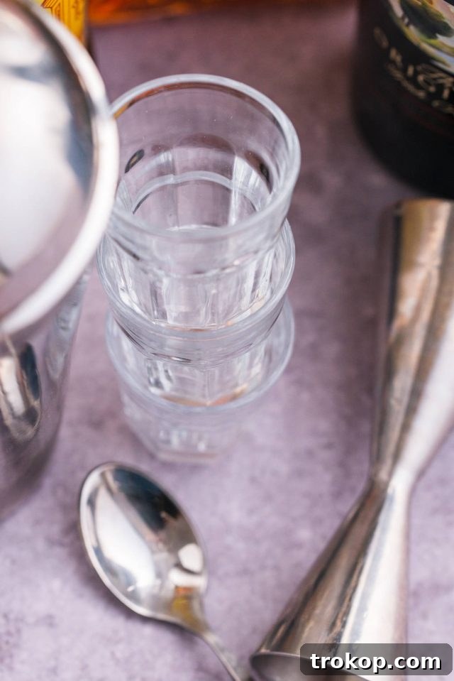 Bartending tools including a jigger for measuring, shot glasses for serving, a bar spoon for layering, and a cocktail shaker for chilling ingredients.