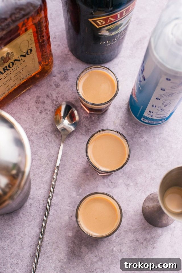 The meticulous process of layering Baileys Irish Cream over the Kahlua and Amaretto base using a bar spoon for a perfectly separated Blow Job Shot.