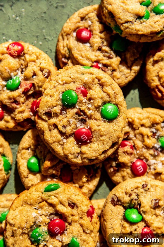 Holiday Cookie Masterclass: Recipes for Delicious Treats and Stunning Displays 23 Colorful Christmas Monster Cookies packed with red and green M&Ms, oats, chocolate chips, and peanut butter.