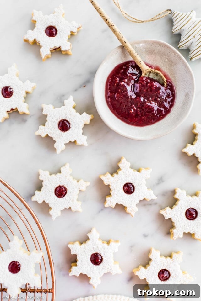 Holiday Cookie Masterclass: Recipes for Delicious Treats and Stunning Displays 29 Elegant Snowflake Linzer Cookies, dusted with powdered sugar and revealing a vibrant raspberry jam filling.