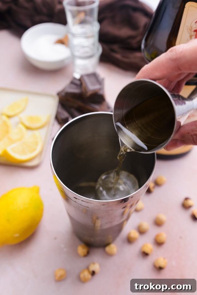 Pouring Frangelico liqueur into a cocktail shaker filled with ice for the Chocolate Cake Shot