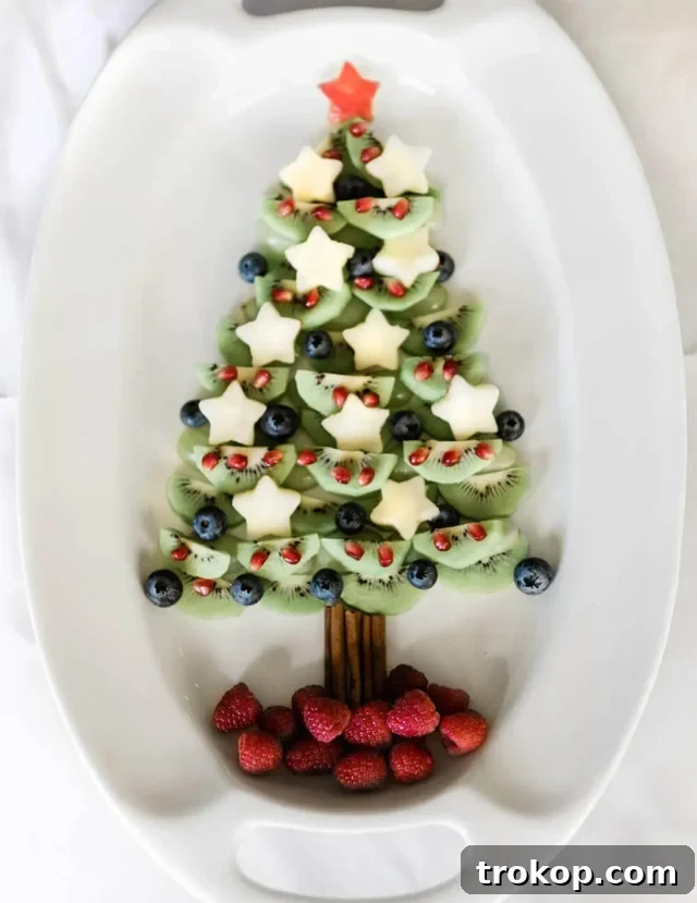 Brilliant Fruit Platter Ideas and Expert Presentation Tips 25 A healthy and festive fruit Christmas tree platter made with layers of green kiwi and grapes, adorned with red raspberries, blueberries, and a star-shaped apple topper, perfect for Christmas parties.