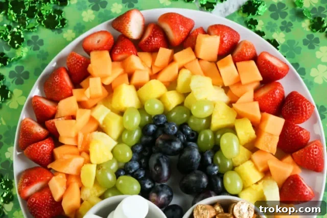 Brilliant Fruit Platter Ideas and Expert Presentation Tips 9 A colorful rainbow fruit platter with arcs of red, orange, yellow, green, blue, and purple fruits, accented with marshmallows as clouds and Rolos as a pot of gold.