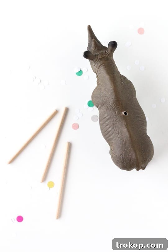 A hand drilling a small hole into the back of a plastic animal figurine, preparing it for the dowel rod.