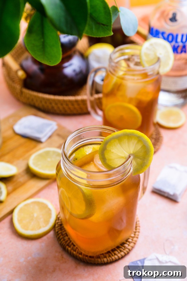 Two glasses of Spiked Arnold Palmer garnished with lemon and mint, served outdoors.