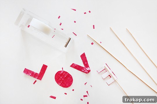 Hand holding a finished DIY fringed cake topper letter 'L' with a kabob stick attached, ready to be placed on a cake.