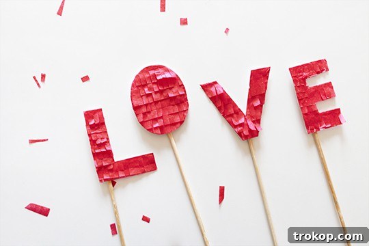 The complete DIY Fringed Love Cake Topper placed on a cake, with individual fringed letters spelling out 'LOVE' in delicate pink and red hues.